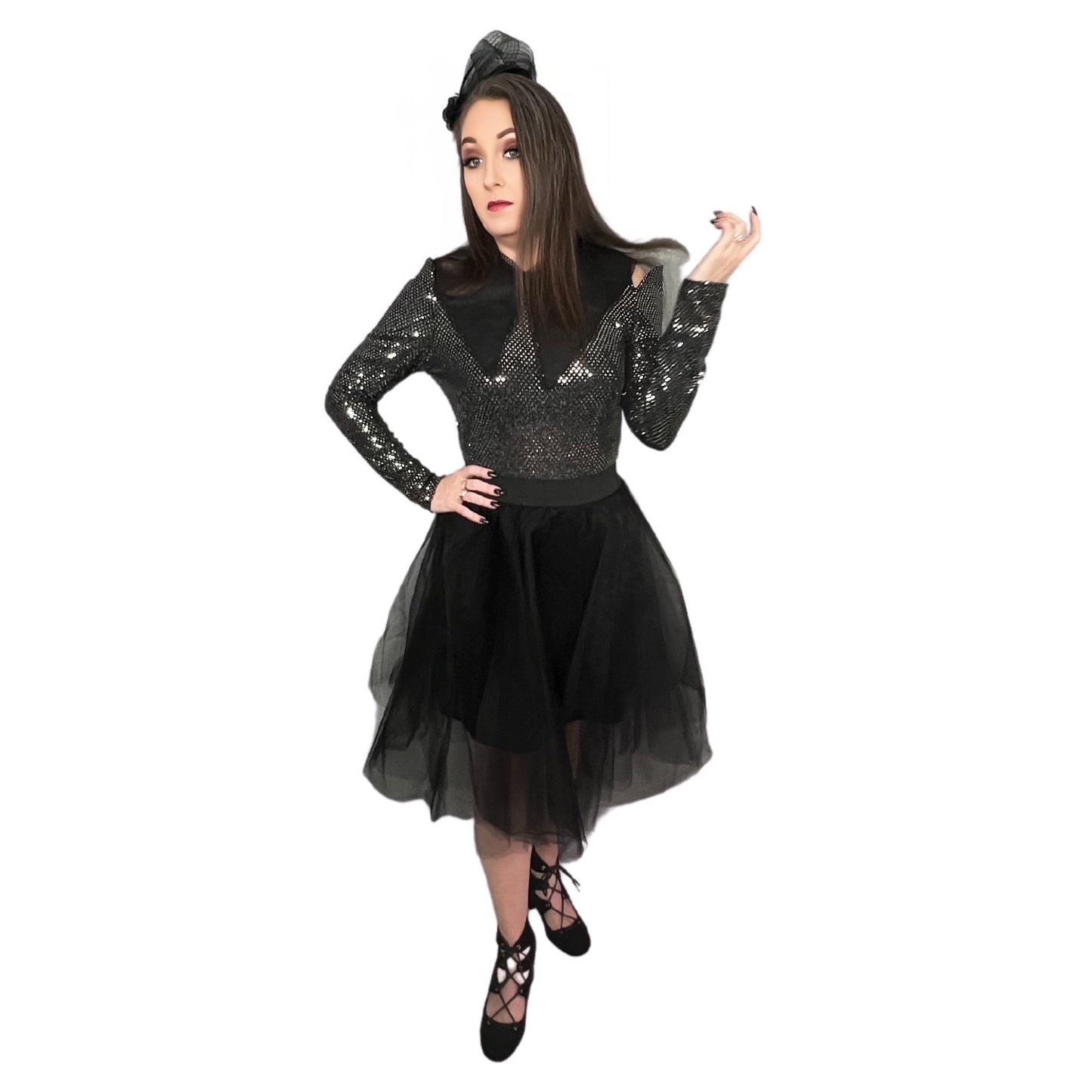 Woman facing forward with one hand on hip and one hand pointed upwards wearing black tulle skirt with elastic waistband, longsleeve shiny body suit, black lace up heels, lapel collar and stylish vintage hat