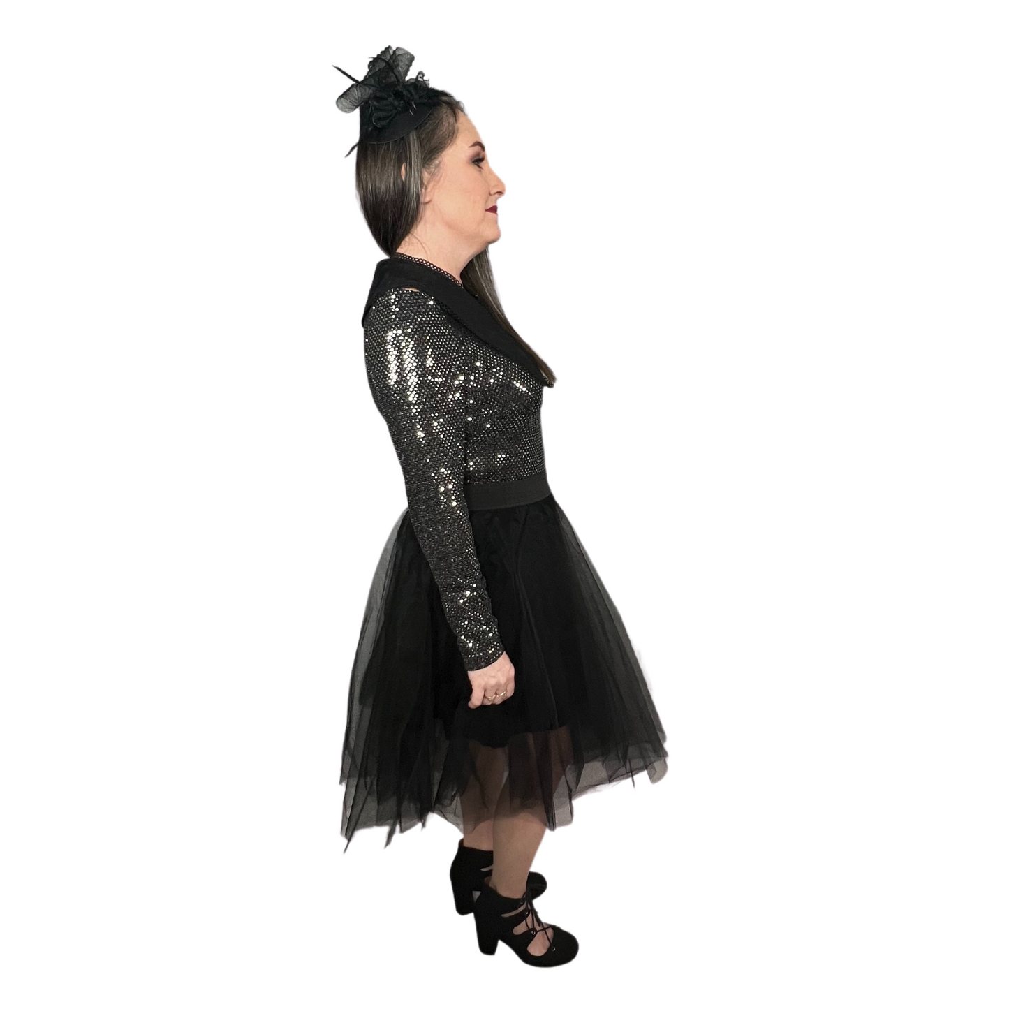 Sideview of woman wearing black tulle skirt with elastic waistband, longsleeve shiny body suit, black lace up heels, lapel collar and stylish vintage hat